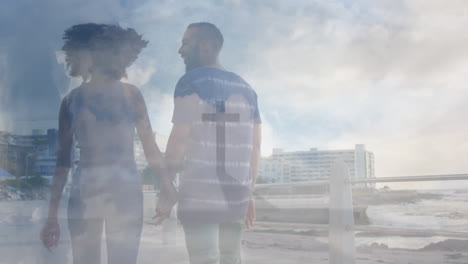 Animation-of-cloudy-sky-and-cross-on-top-of-mountain-over-diverse-couple-walking-holding-hands