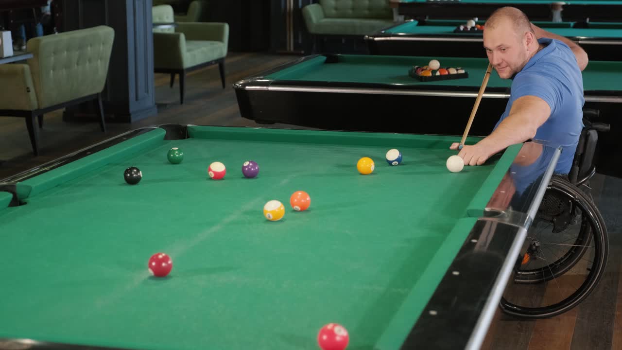 Adult men with disabilities in a wheelchair play billiards in the club