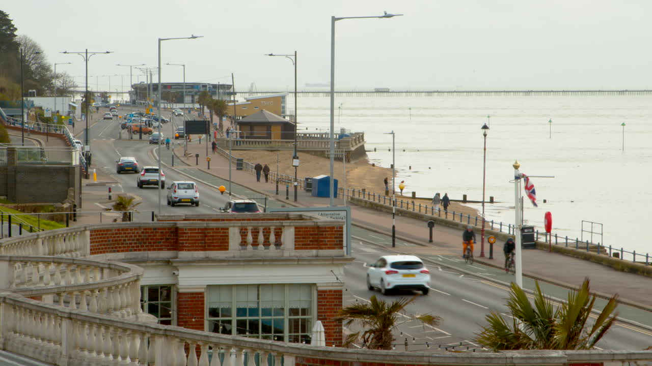 Coastal road with flags, beach waves and pier in the distance.