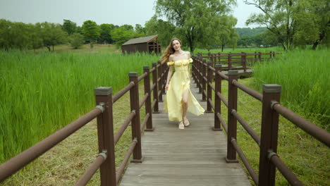 Stylish-young-woman-wearing-sundress-walking-down-park-boardwalk,-away-from-camera,-tilt-up