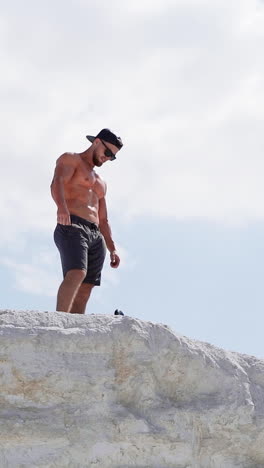 shirtless athlete in cap and glasses on mountain. view from below on a sportsman standing on the top of white hill. vertical video