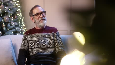 close up of joyful surprised old grandpa receiving christmas gift from caring teen boy while sitting in decorated room near glowing tree