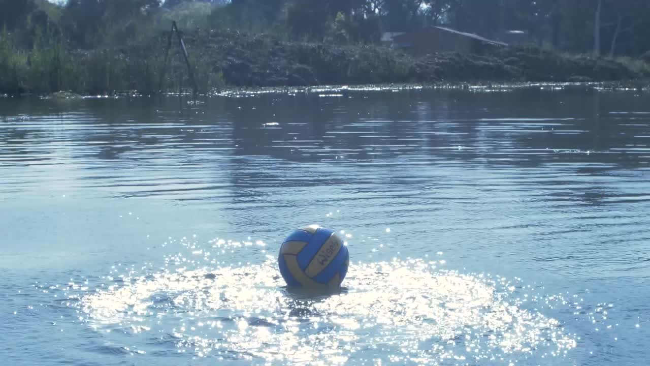Polo ball hitting shimmering water on dam in slow motion