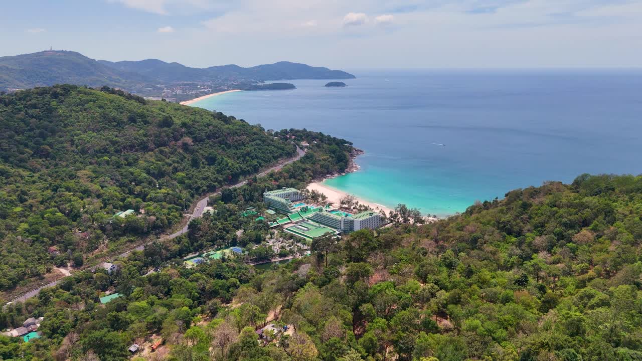 Drone footage captures Phuket's lush greenery and turquoise waters, showcasing a luxury resort nestled along the coastline under bright daylight