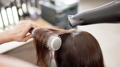 Peluquera-Caucásica-Peinando-El-Pelo-Largo-Del-Cliente-Con-Secador-De-Pelo-Y-Cepillo,-Cámara-Lenta