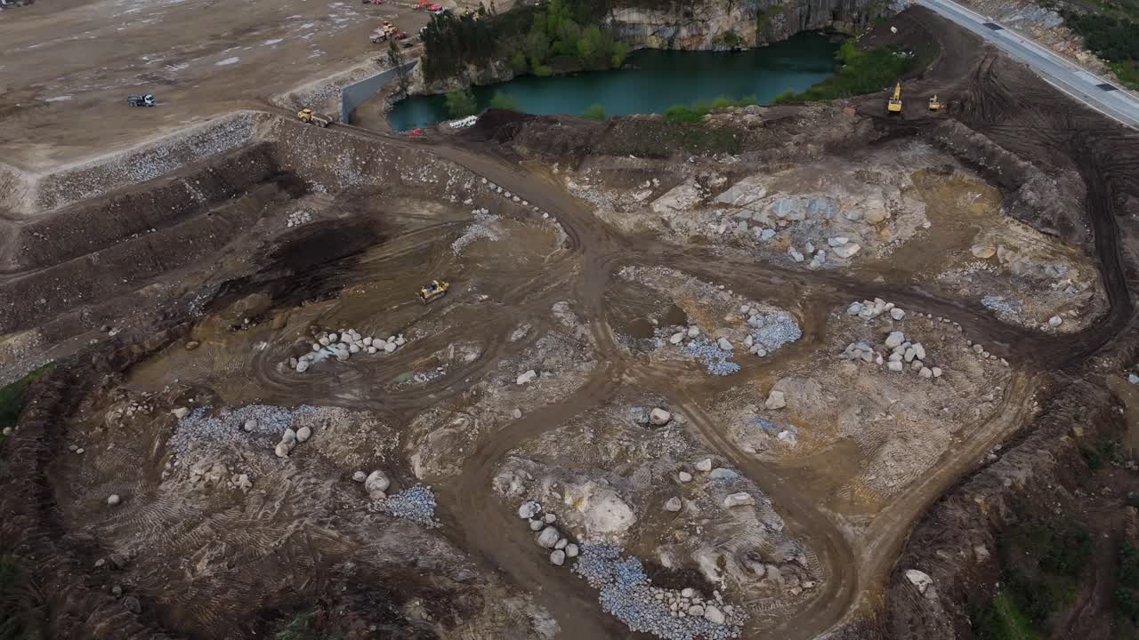 aerial - construction machinery active in rocky quarry with turquoise lake in background