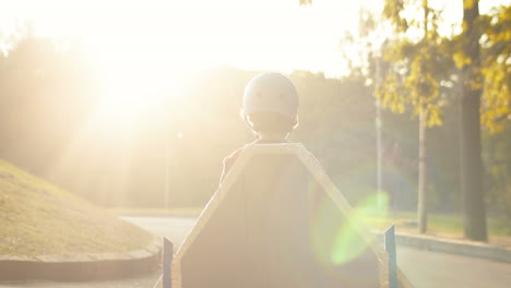 back view of a little boy in helmet and red sweater with cardboard airplane wings standing outdoor on sunny day and playing as a pilot