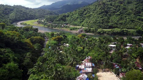 birds soar over tropical asian village in forest by river bank, aerial dolly