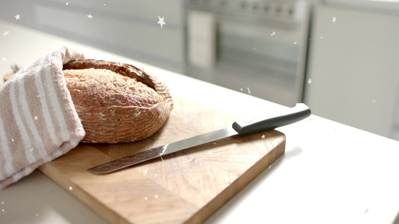 Camera starting slow pan, revealing round loaf, towel, knife; stars drifting, showing kitchen scene
