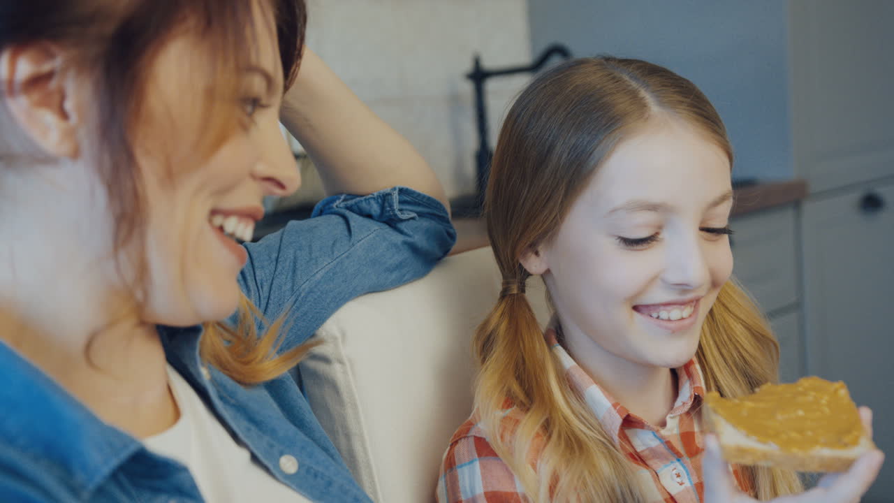 예쁜 금발 십대 소녀가 그녀의 아름다운 어머니와 이야기하고 땅콩 버터로  ⁇ 을 먹고 있습니다. 가까이. 실내