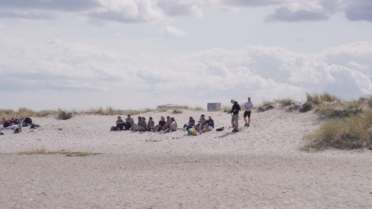 Group of people sit on sandy dune at Amager beach in cloudy day, Copenhagen