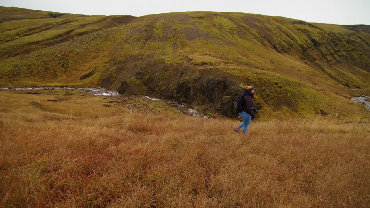 young woman wanders through a meadow near a waterfall and stream in endless space and freedom
