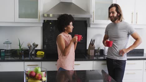 pareja de raza mixta sosteniendo una taza de café hablando entre sí en la cocina en casa