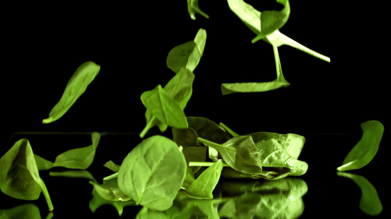 Foglie fresche di spinaci verdi che cadono su una superficie nera riflettente