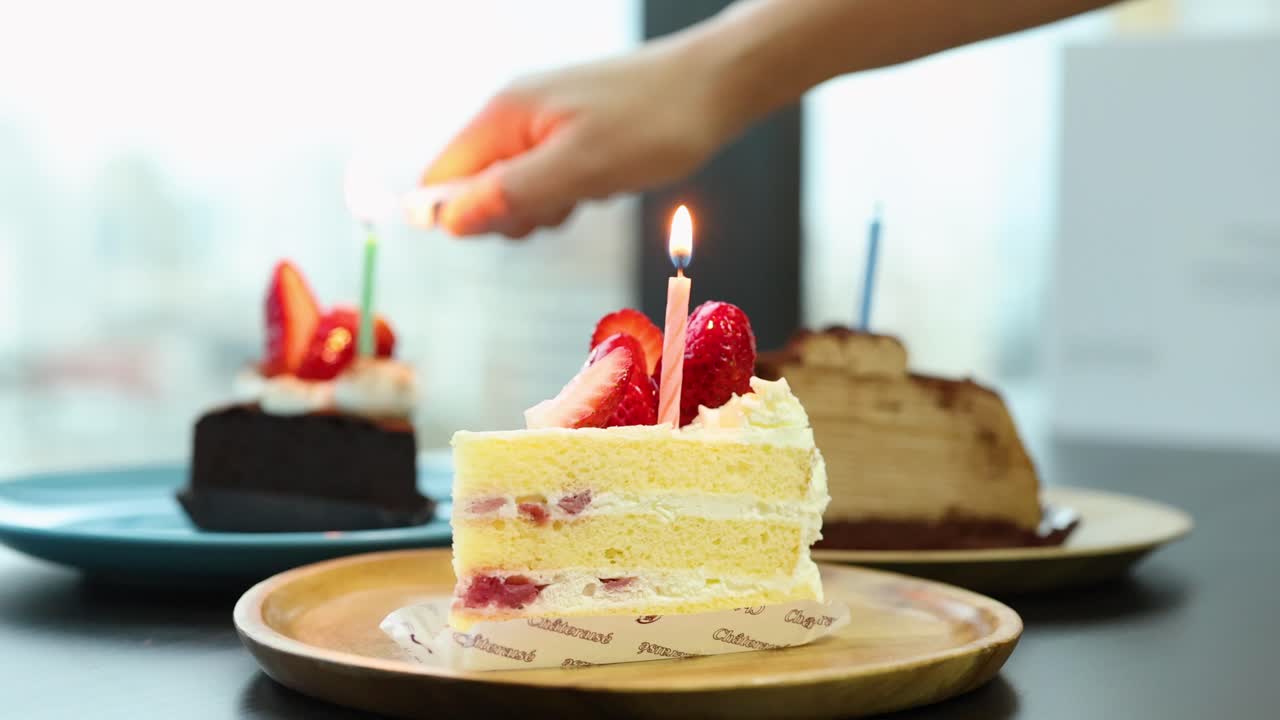 Hand lights candle on strawberry shortcake slice, natural daylight, shallow focus, steady camera