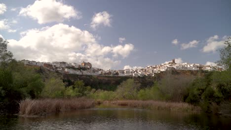 pan across small pond looking out towards white-washed spanish village on hill