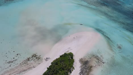 top-down fly over small deserted sandy island with palm trees, small boat and people