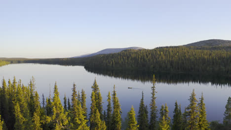 Aerial-view-over-forest-to-a-lake-with-a-small-canoe-in-a-perfectly-still-water-with-forest-and-hills-in-the-background