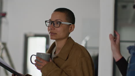 woman in a brown jacket talking to a colleague in an office