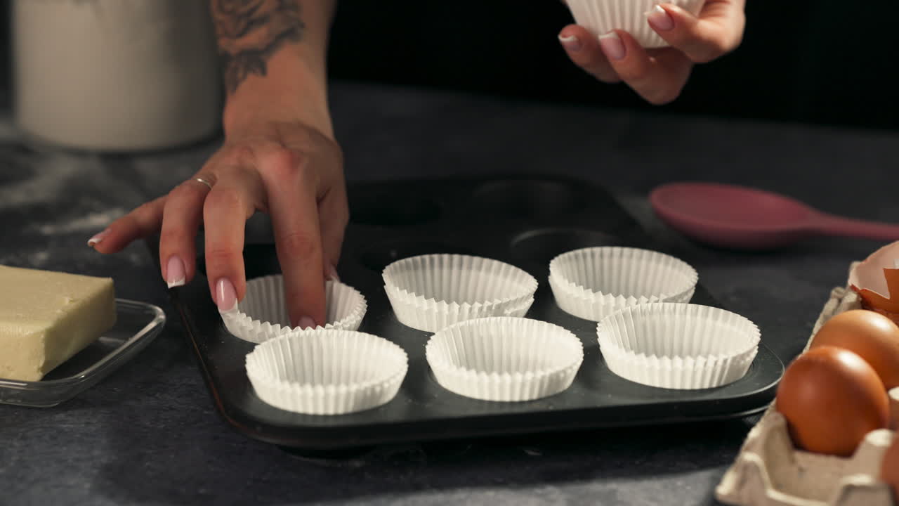 Medium static of person placing cupcake liners into dark tray on table, slow motion