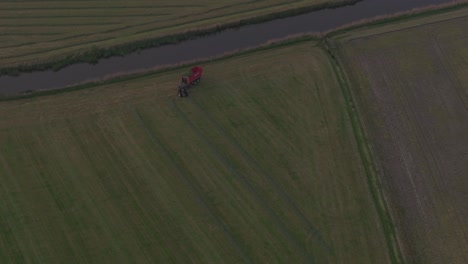 Tractor-driving-on-meadow-in-the-netherlands-during-sunset,-aerial