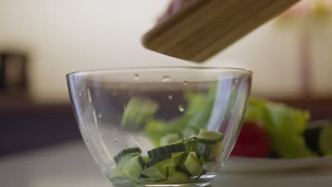 pouring juicy cucumber slices into glass bowl on table