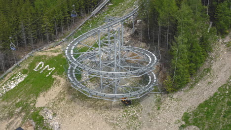 4k-luftaufnahme einer riesigen achterbahnschleife einer extremen outdoor-fahrt in den bergen von dolní morava, tschechische republik, die an einem hang mit bäumen herumsteht