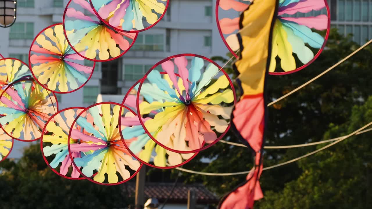 Vibrant pinwheels twirl energetically against a backdrop of city buildings and greenery.