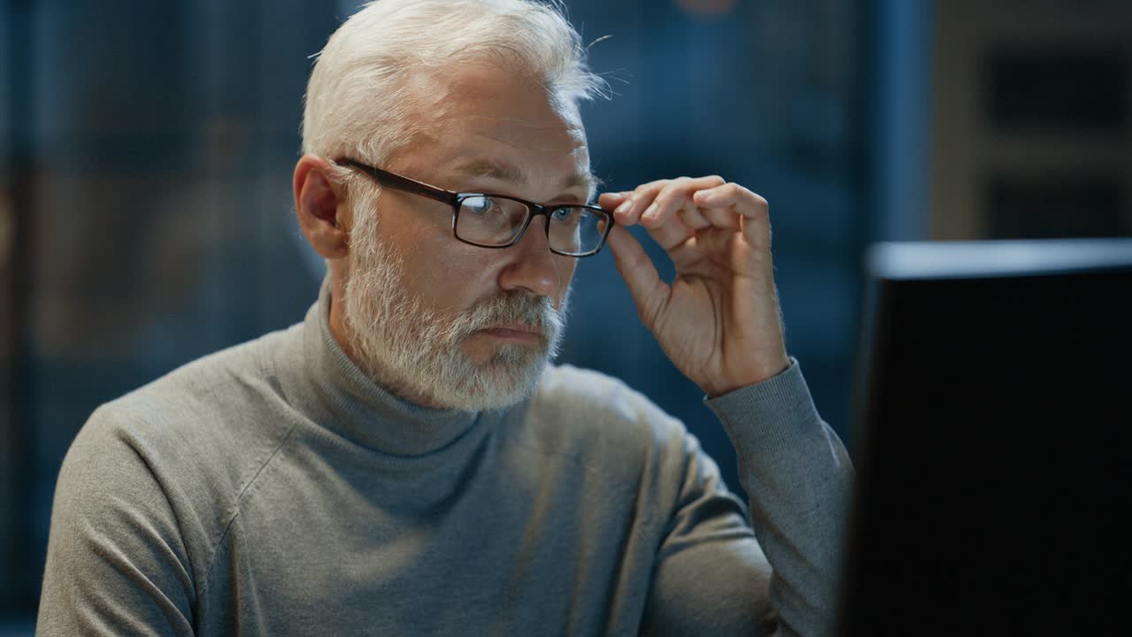 Portrait of the Handsome and Successful Middle Aged Bearded Businessman Working at His Desk Using Laptop Computer. Smiles at Camera. Working at Night from Cozy Home Office / Studio with Window