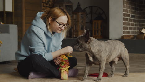 red haired woman caresses her bulldog dog while they are sitting on the floor in the living room at home