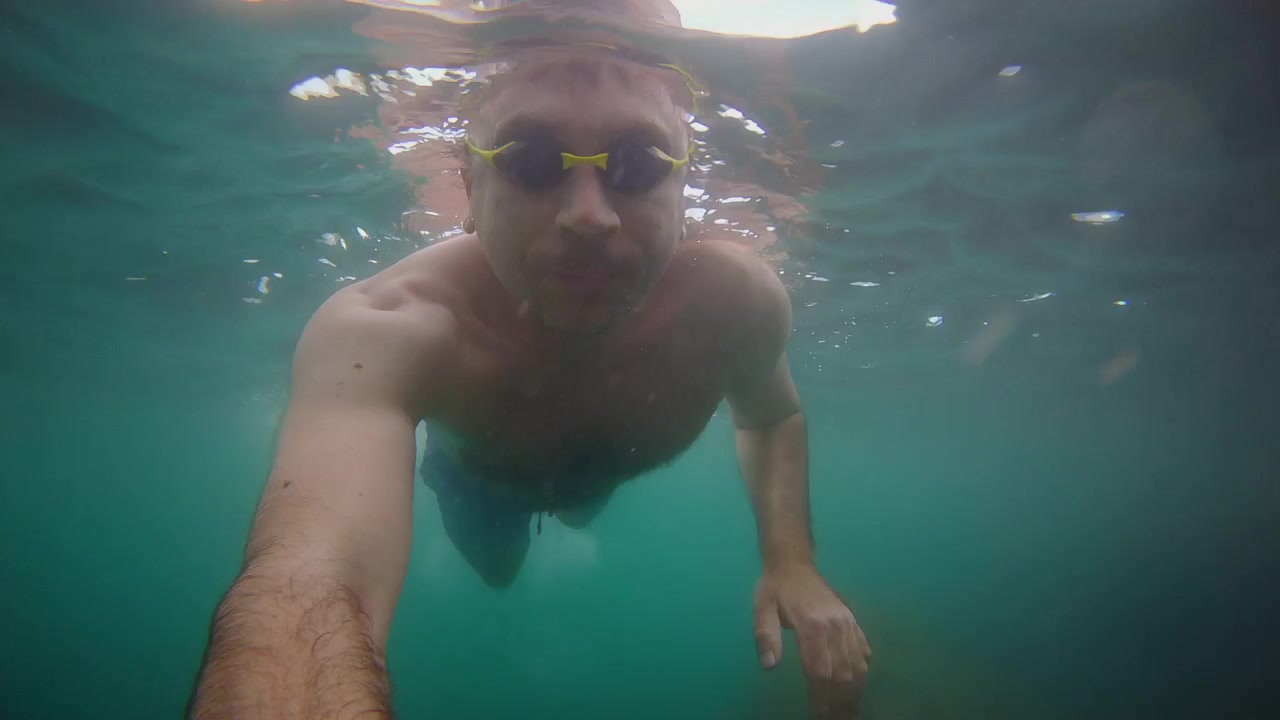 Riprese subacquee in autoscatto di un uomo che nuota in acque oceaniche limpide e blu mentre indossa occhialini da nuoto.