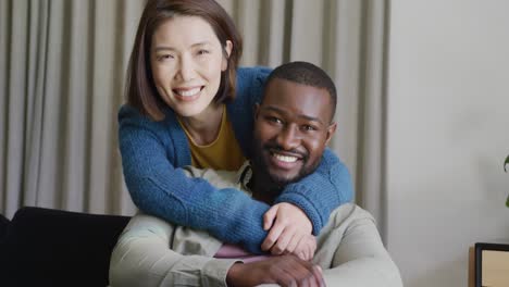 video portrait of happy diverse couple embracing and smiling to camera at home