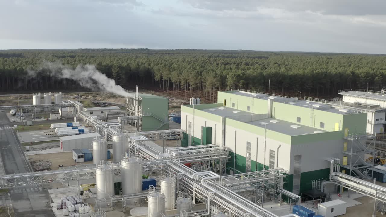 Drone footage flying over manufacturing plant showing buildings, numerous storage tanks, pipes, and steam emissions, Castets, France