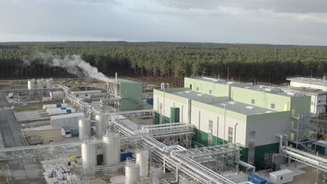 drone footage flying over manufacturing plant showing buildings, numerous storage tanks, pipes, and steam emissions, castets, france