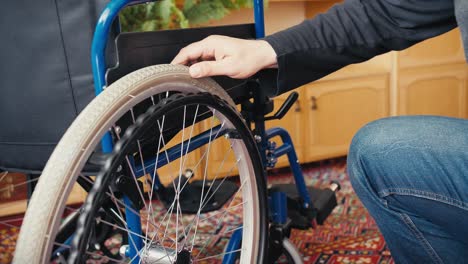 A-man-in-jeans-and-a-black-and-gray-T-shirt-checks-the-amount-of-air-in-the-tires-of-a-wheelchair