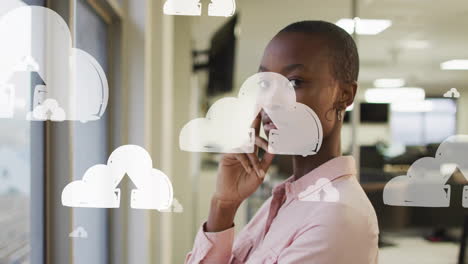 animación de iconos de nube digital con flechas sobre mujer de negocios afroamericana en la oficina