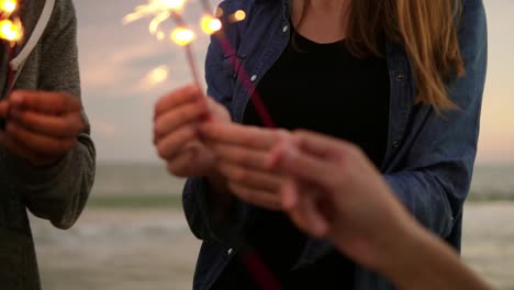 Close-Up-view-of-young-people-holding-bengal-lights-during-evening-standing-by-the-sea-during-sunset.-Slow-Motion-shot