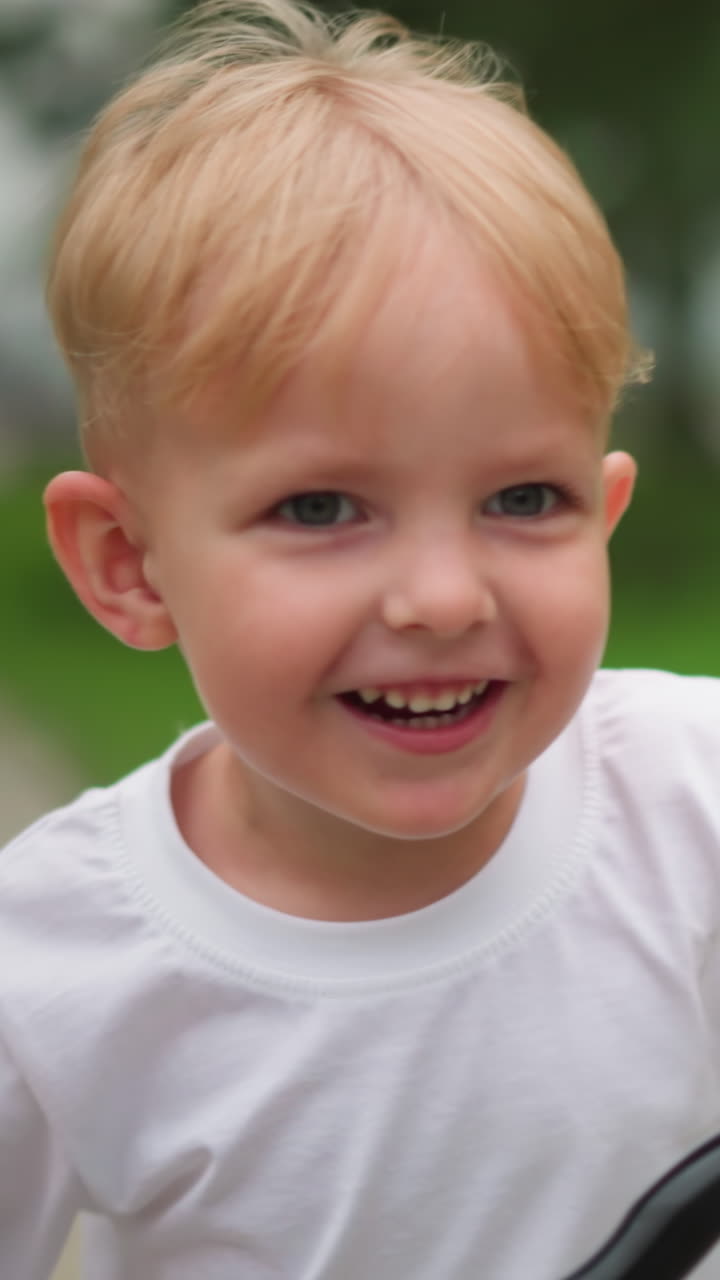 un niño alegre monta su bicicleta con una gran sonrisa en la cara, el fondo presenta un borrón de vegetación