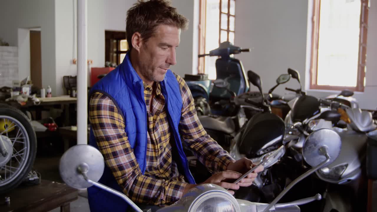 mecánico masculino que usa una tableta digital en un garaje de reparación de motocicletas 4k