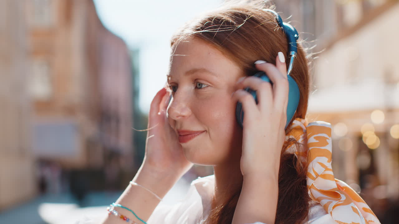 Happy young child girl in wireless headphones choosing listening music dancing outdoors city street