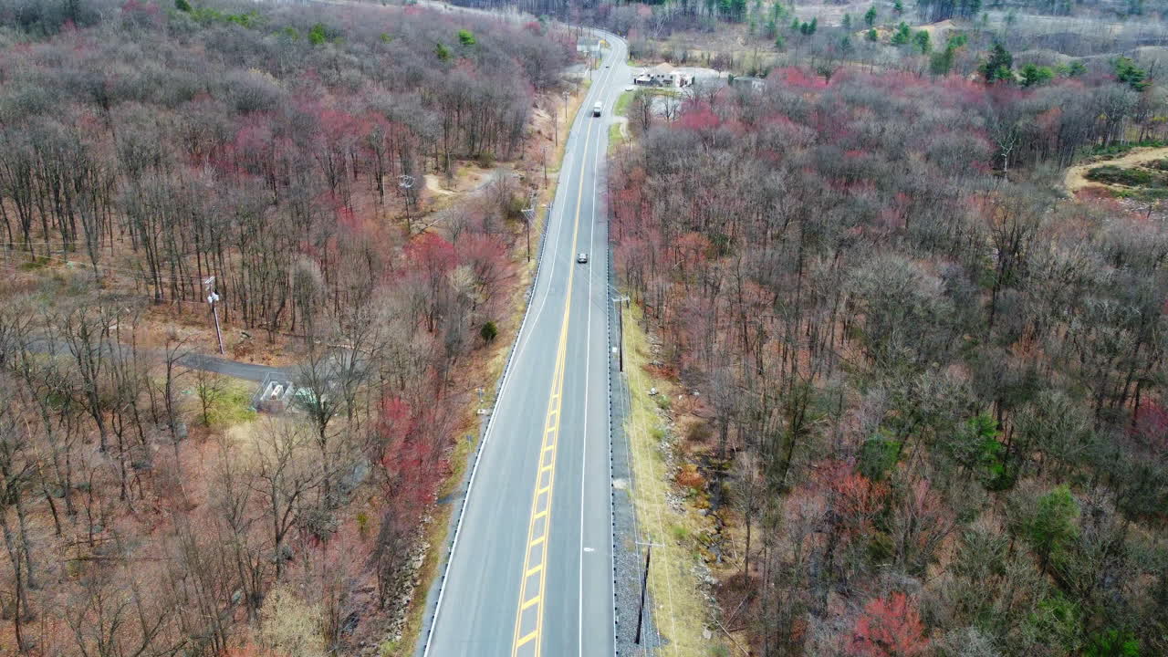 A drone shot follows a winding country road in Schuylkill County as cars and trucks pass through a winter landscape. Bare trees line the route, creating a peaceful, seasonal transportation scene.