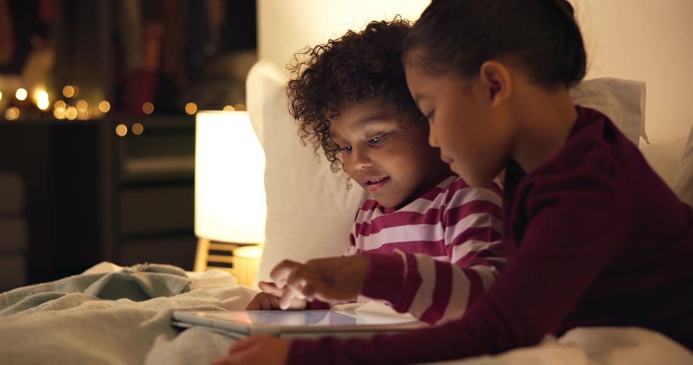Two Children Using a Tablet Together in Bed at Night