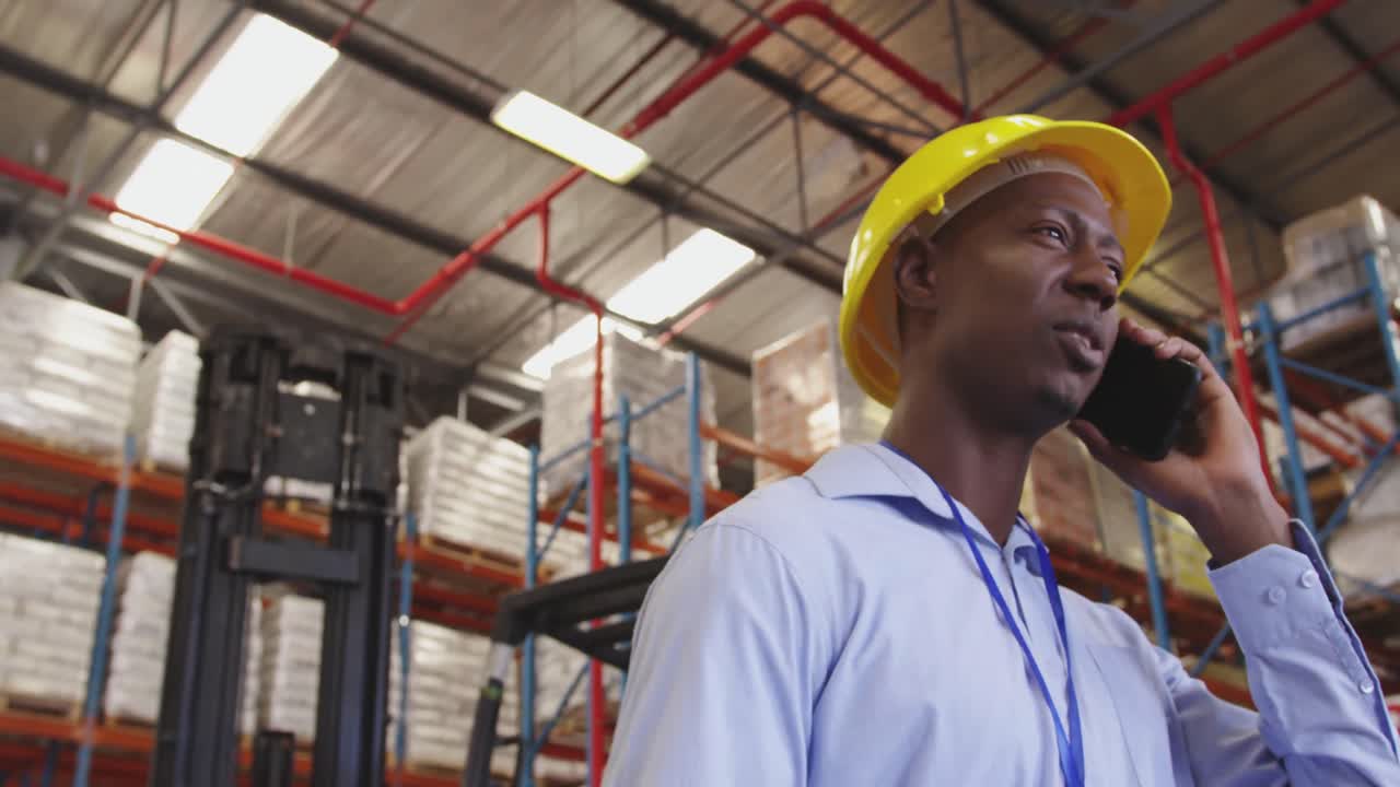 Young man wearing a hard hat using smartphone in a warehouse 4k