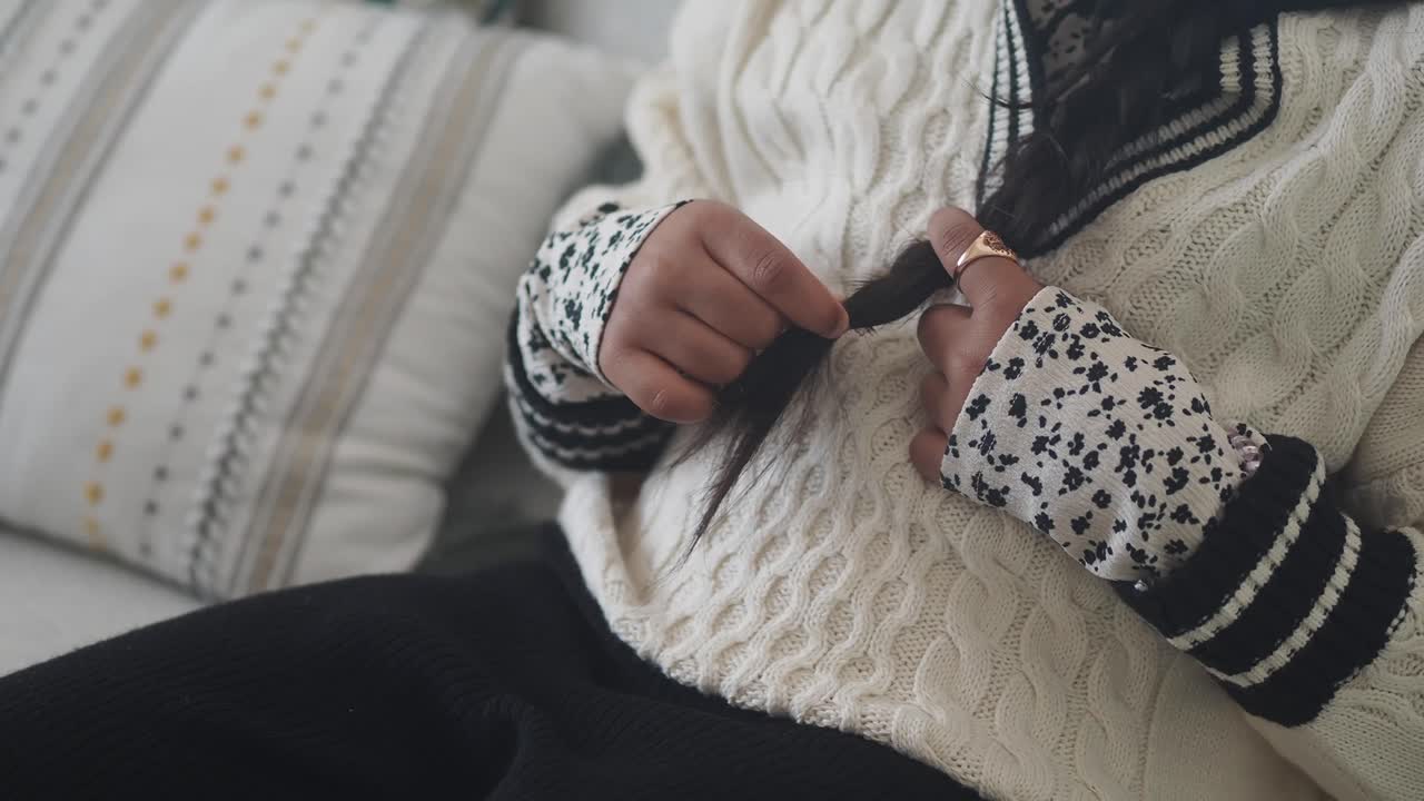 A person in a sweater with a braid is relaxing on a couch