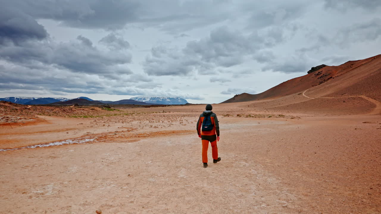 Ampia inquadratura posteriore di un viaggiatore solitario che esplora il paesaggio dell'area geotermica di Hverir sul monte Námafjall, Islanda. Spedizione solitaria. Terreno aspro e suggestivo