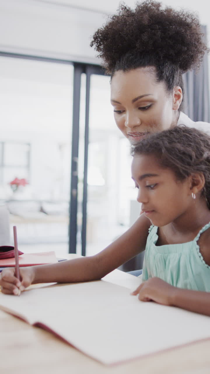 Vertical video of biracial mother and daughter sitting at table, doing homework, slow motion