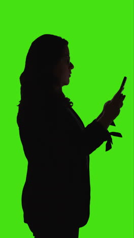 vertical video side view silhouetted shot of woman using mobile phone standing against green screen