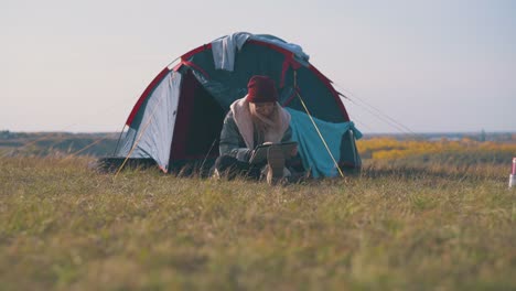 woman in jacket and hat uses tablet at tent in evening