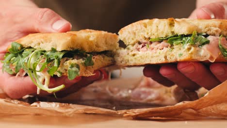 mortadella ham sandwich, traditional italian focaccia filled with thin pesto slices of mortadella, served by chef man in cafe restaurant. macro of traditional italian spanish tapas antipasti.