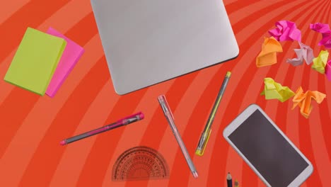 Animation-of-laptop-and-office-items-over-orange-spinning-stripes